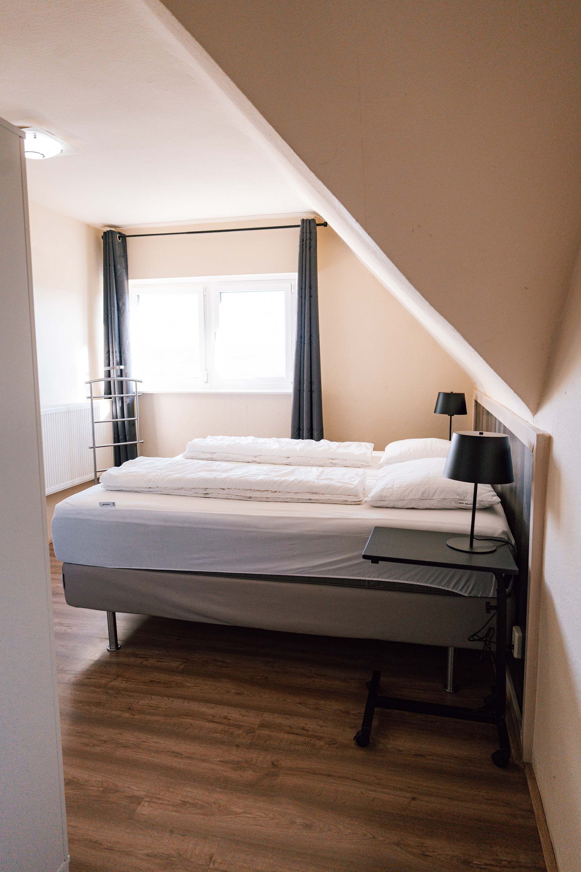 Un dormitorio con cama, mesita de noche, lámpara, ventana con cortinas y radiador.
