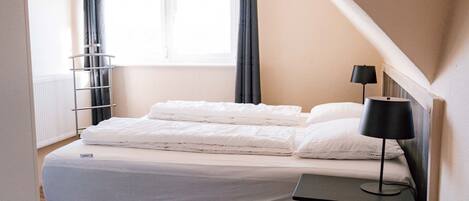 Un dormitorio con cama, mesita de noche, lámpara, ventana con cortinas y radiador.