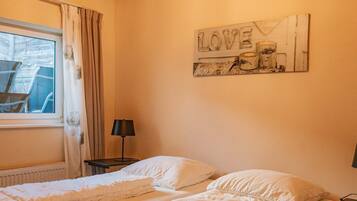 A double bed with white bedding, a chandelier, a window with curtains, and a wall decoration with the word 'LOVE'.