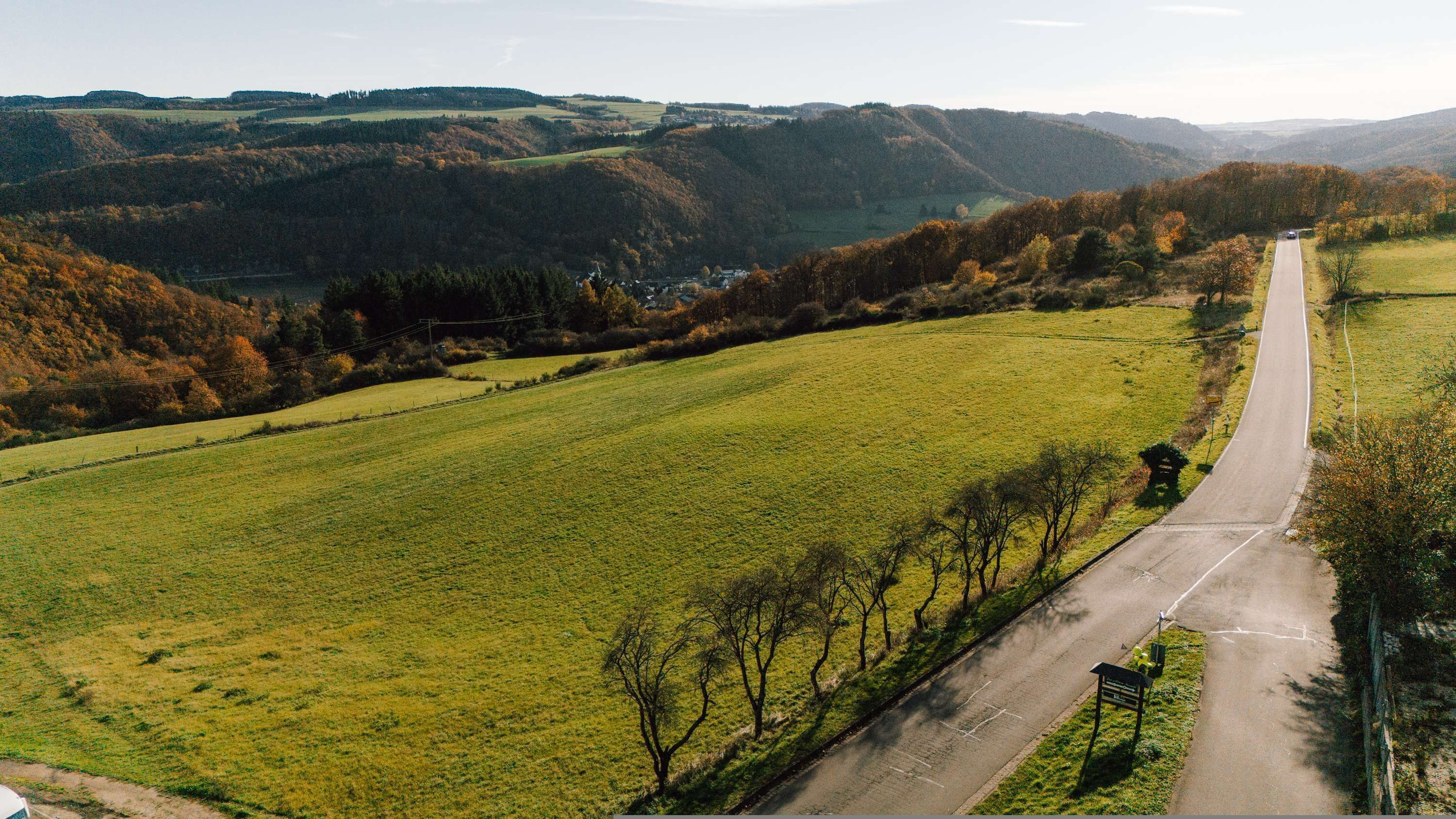 Eine ländliche Straße mit Feldern und Hügeln im Hintergrund.