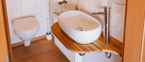 A bathroom with a white toilet, a white sink, a mirror, and a shelf with glasses.