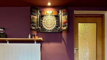 A room with a dartboard, a radiator, a wooden door, and a carpet with numbers.
