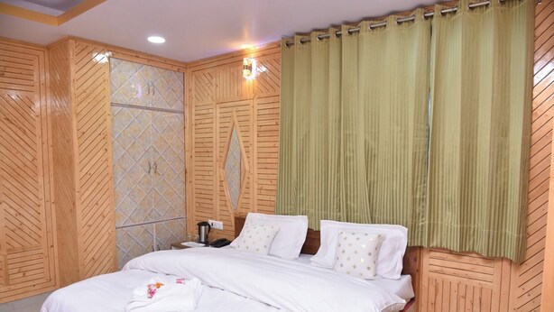 A neatly made bed with white linens, a wooden headboard, and a green curtain. - Sarahan Holliday Inn (Rampur)