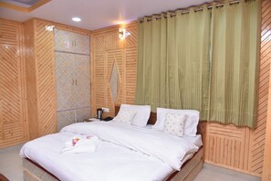A neatly made bed with white linens, a wooden headboard, and a green curtain. - Sarahan Holliday Inn (Rampur)