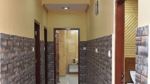 A hallway with a tiled floor, a wooden door on the right, and a bathroom visible through an open door at the end. - Sarahan Holliday Inn (Rampur)