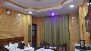 A hotel room with a bed, two chairs, a table, a kettle, and a ceiling light. - Sarahan Holliday Inn (Rampur)