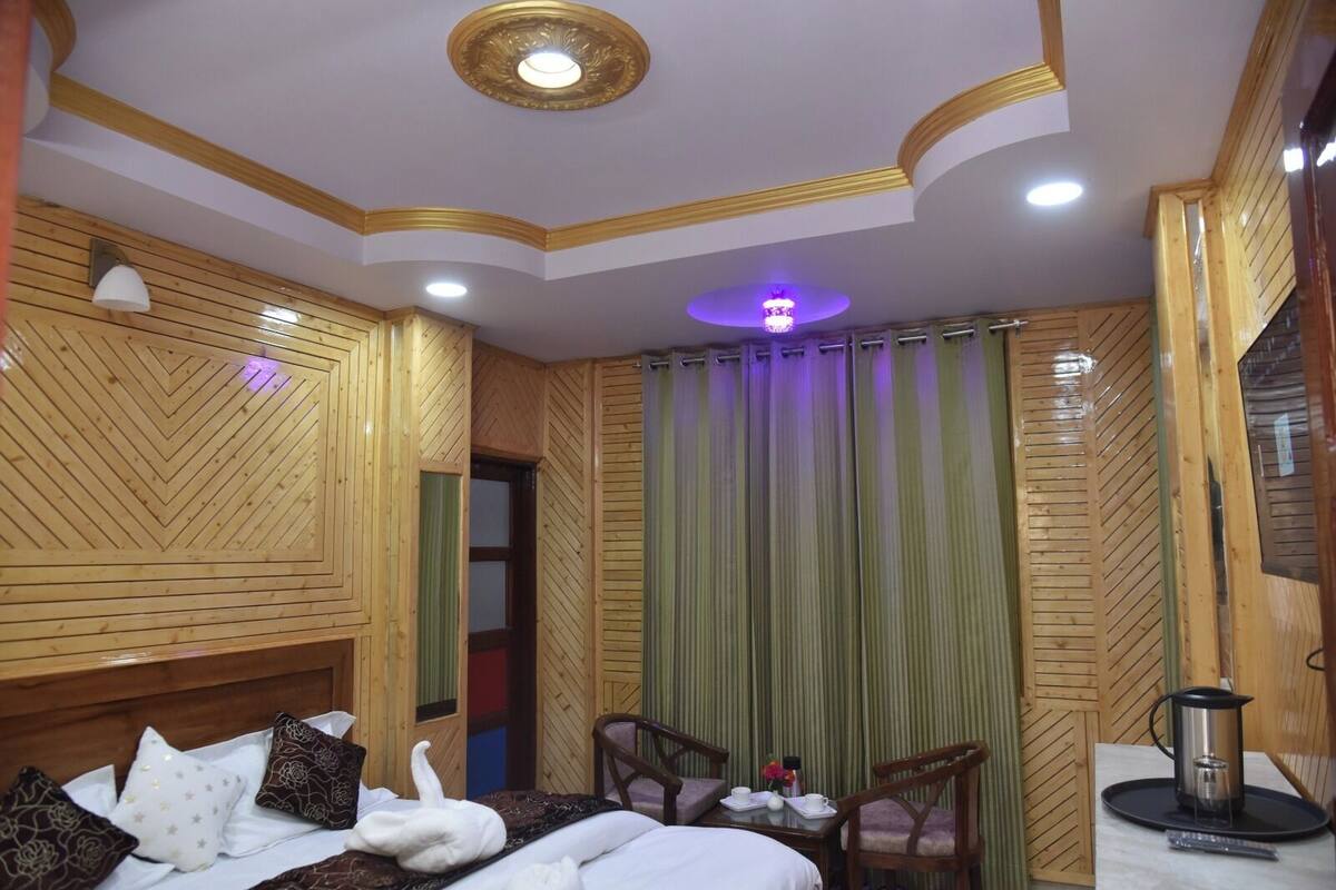 Una habitación de hotel con una cama, dos sillas, una mesa, un hervidor y una lámpara en el techo.