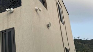 En bygning med en struktureret facade, et vindue med sort ramme og en lille, fastmonteret lysarmatur.