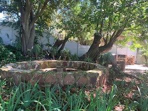 Una estructura circular de piedra rodeada de vegetación, con árboles y plantas al fondo.