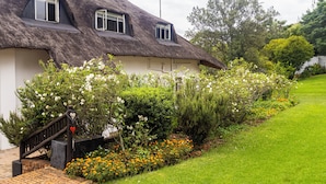 Una casa con techo de paja y una escalera de ladrillo que conduce a una puerta, rodeada por un jardín con diversas plantas y flores.