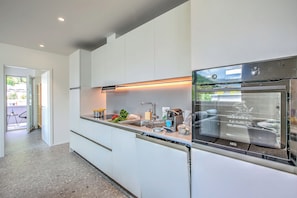 A modern kitchen with a built-in oven, a dishwasher, and a countertop with various kitchen items. - Urban Maggiolina Sunset With Terrace & Mountain Views (Locarno)