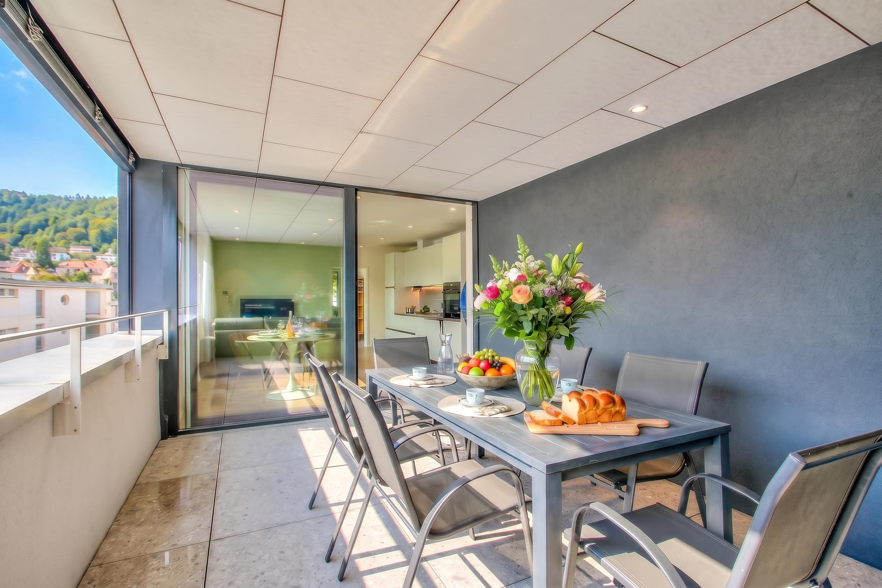 A modern dining area with a table set for two, a vase of flowers, and a bowl of fruit.