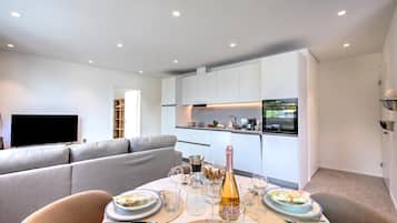 A modern living room with a dining area, a flat-screen TV, and a kitchen with white cabinets and a built-in oven.
