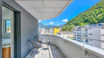 A balcony with a view of mountains, a yellow building, and a modern building with solar panels.