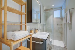 A modern bathroom with a glass shower enclosure, a white sink, and wooden shelves with towels. - Urban Maggiolina Sunset With Terrace & Mountain Views (Locarno)