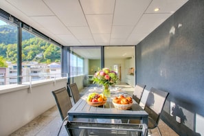 Un comedor con una mesa preparada para cuatro personas, un jarrón de flores y un frutero.