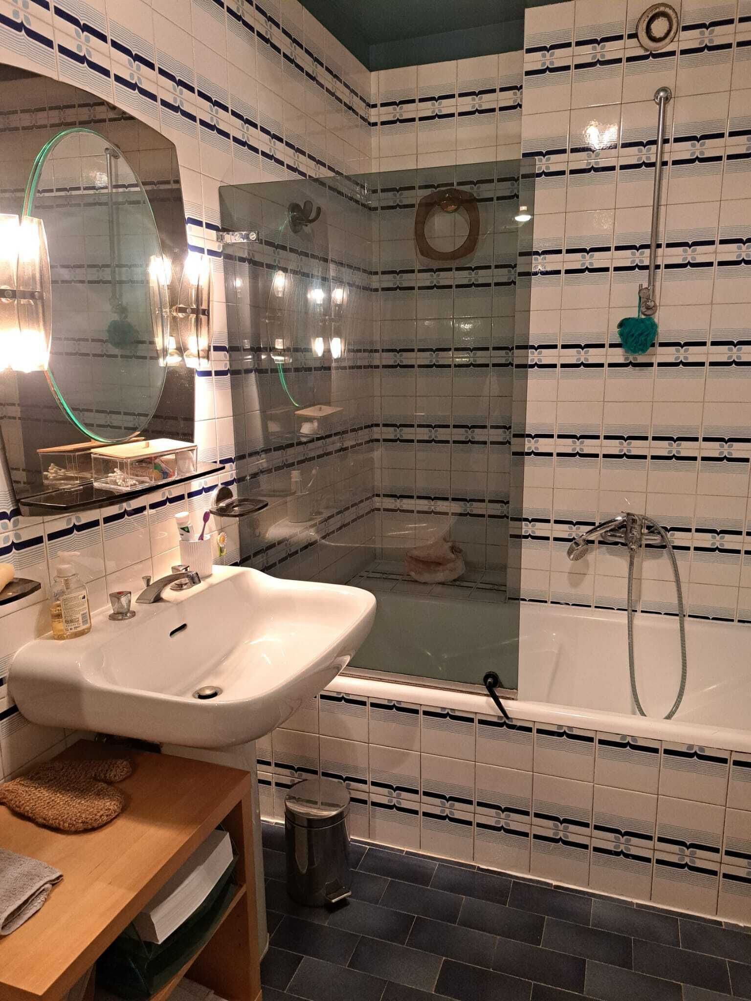A bathroom with a sink, mirror, shower, and tiled walls.