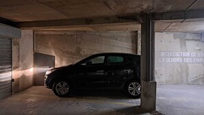A black car parked in a dimly lit underground parking garage with concrete walls and a metal door. - MONACO Fantastic seaview - 2 bedrooms- 110m² - AC (Roquebrune Cap Martin)