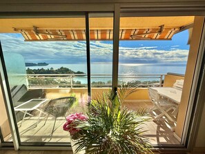 Un balcon avec vue sur la mer, une table, des chaises et une plante en pot.