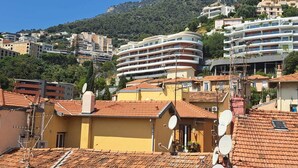 A coastal town with terracotta-roofed buildings, a prominent curved white building, and a mountainous backdrop. - MONACO Fantastic seaview - 2 bedrooms- 110m² - AC (Roquebrune Cap Martin)
