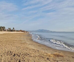 Ein Strand mit sandigem Ufer, ruhigem Wasser und Bergen in der Ferne.