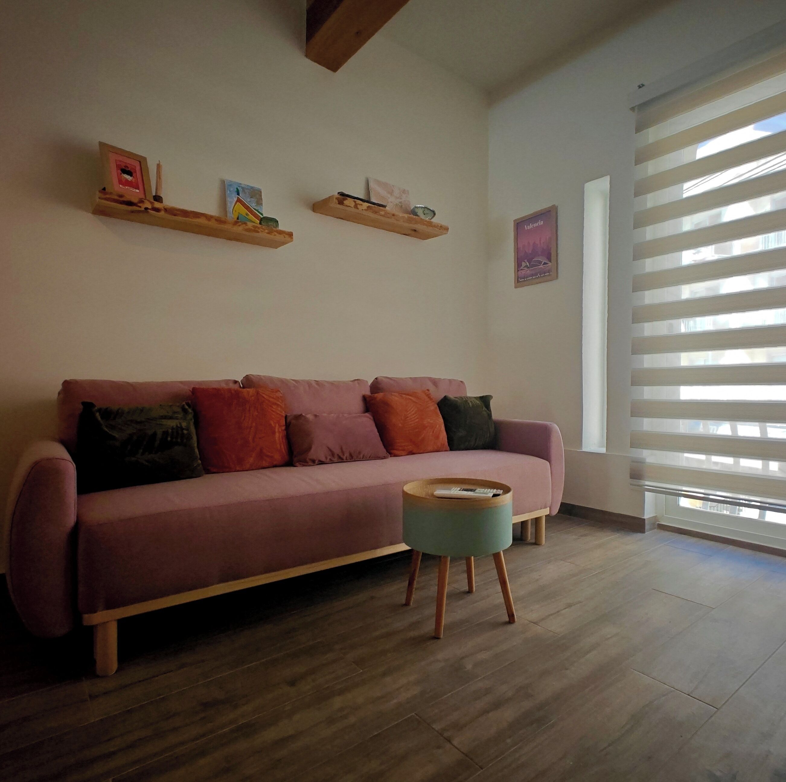 A living room with a pink sofa, wooden floor, and a window with blinds.