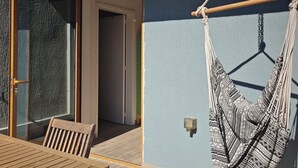 Ein Holztisch mit Stühlen vor einem Gebäude, dessen Wand blau ist, eine Hängematte und eine Tür zu einem Innenraum.