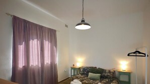 Ein Schlafzimmer mit einem Bett, zwei Nachttischen, einer Pendelleuchte, einem Kleiderhaken und einem Schreibtisch.