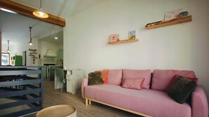 Ein Wohnzimmer mit einem rosafarbenen Sofa, einem runden Holztisch und einer Küche im Hintergrund.