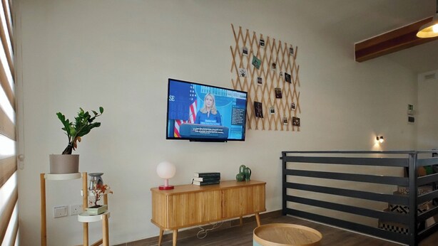Ein modernes Wohnzimmer mit Fernseher, Holzmöbeln, einer Wandverkleidung und einer Geländer.