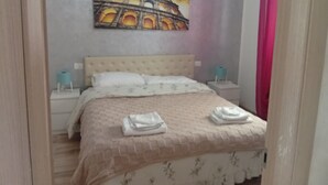 A bedroom with a bed, a nightstand, a wall-mounted painting of the Colosseum, and a red curtain.