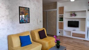 A living room with two yellow sofas, a coffee table, a TV, and a painting on the wall.