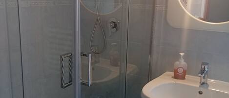 A bathroom with a glass-enclosed shower, a white sink, and a round mirror.