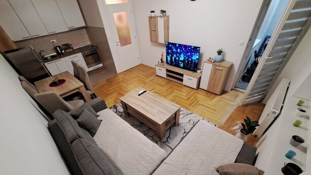 Una sala de estar moderna con sofá, mesa de centro, televisor, zona de cocina y una escalera.