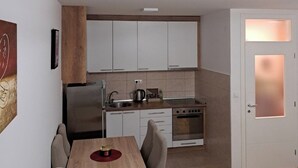 Una cocina funcional con armarios blancos, estufa y lavaplatos. Hay una mesa de comedor con sillas y piso de madera.