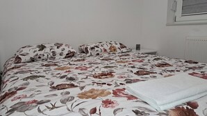 Una cama con ropa de cama floral, una mesita de noche con lámpara y una ventana con persianas.