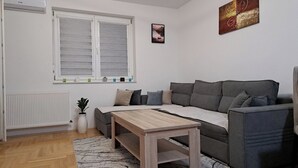 Una sala de estar moderna con un sofá gris, una mesa de centro de madera, un radiador, una planta en maceta y una ventana con persianas.