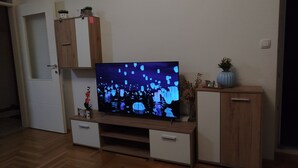 Una sala de estar con televisor de pantalla plana sobre un mueble de madera, una puerta blanca y un reloj de pared.