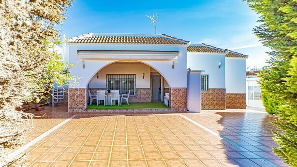 A two-story house with a tiled driveway, a patio with outdoor furniture, and a clear blue sky.