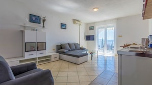 Una sala moderna con un sofá gris, un televisor y una zona de cocina con una cafetera.