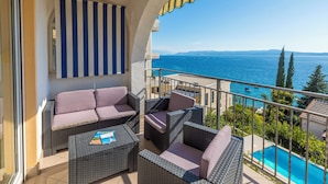 Un balcón con muebles de mimbre, una cortina a rayas y vista al mar.