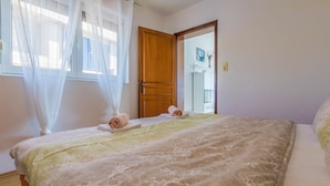 Un dormitorio con una cama, una puerta de madera y una ventana con cortinas traslúcidas.