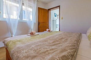 A bedroom with a bed, a wooden door, and a window with sheer curtains. - Beautiful apartment with covered balcony, sea view of Krk and pool (Crikvenica)