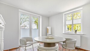 Ein Zimmer mit einem runden Tisch, vier Stühlen, einem weißen Heizkörper und einem Fenster mit Rollläden.