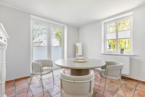 A room with a round table, four chairs, a white radiator, and a window with blinds.