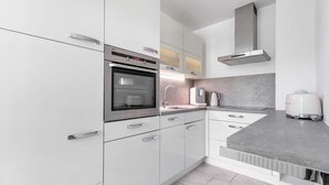 Eine moderne Küche mit weißen Schränken, einem Edelstahlbackofen, einer eingebauten Mikrowelle und einer grauen Arbeitsplatte.