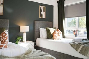 Ett hotellrum med två sängar, en sänglampa, en liten växt och ett fönster med gardiner.