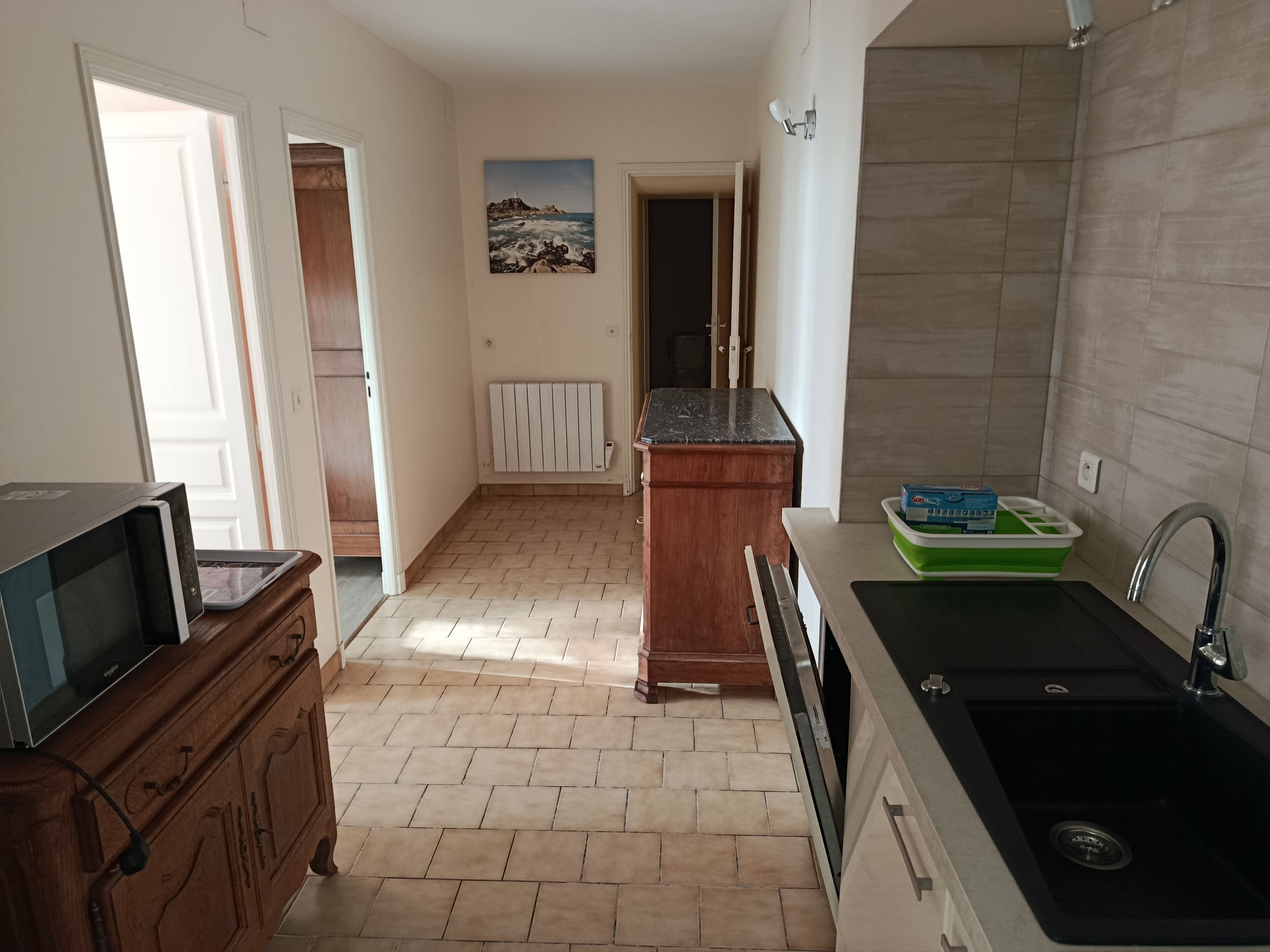 A kitchen with a microwave, wooden cabinets, a sink, and a painting on the wall.