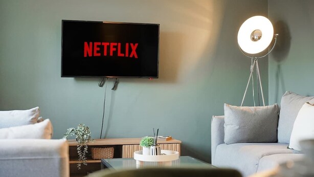 Olohuoneessa on litteänäyttöinen televisio, jossa näkyy Netflix, moderni lattiavalaisin ja sohva.