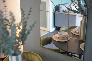 Un coin repas avec une table ronde, des chaises et un miroir qui reflète la pièce.